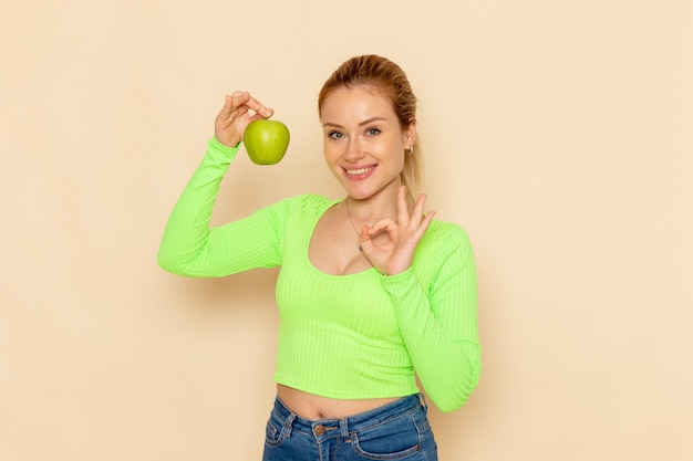 Gratis foto vooraanzicht jonge mooie vrouw in groen shirt met groene verse appel lachend op crème bureau fruit model mellow vrouw