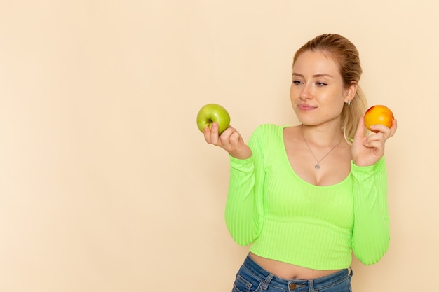 Vooraanzicht jonge mooie vrouw in groen shirt met paar appels op crème muur fruit model vrouw mellow