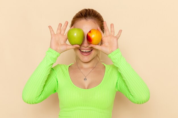 Vooraanzicht jonge mooie vrouw in groen shirt met paar verse appels die haar ogen op crème muur fruit model mellow vrouw bedekken