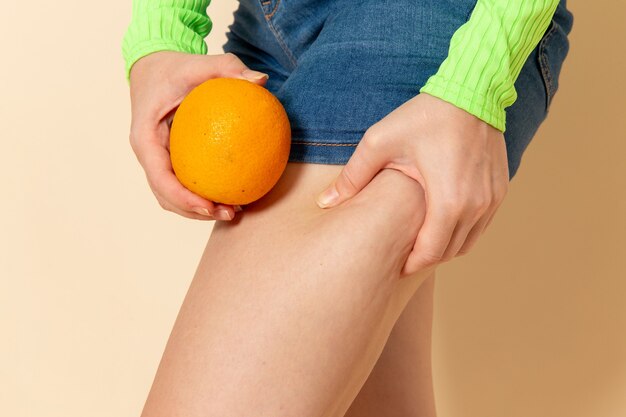 Vooraanzicht jonge mooie vrouw in groen shirt met sinaasappel op crème muur fruit model mellow vrouw