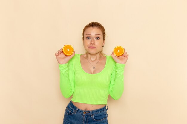 Gratis foto vooraanzicht jonge mooie vrouw in groen shirt met stukjes sinaasappel op de crème muur fruit model mellow vrouw