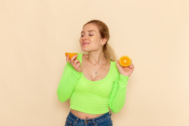 Vooraanzicht jonge mooie vrouw in groen shirt met stukjes sinaasappel ruiken op de crème muur fruit model mellow vrouw