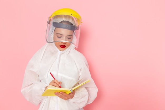 Vooraanzicht jonge mooie vrouw in speciaal wit pak met beschermende helm aantekeningen op de roze ruimtepak vrouw