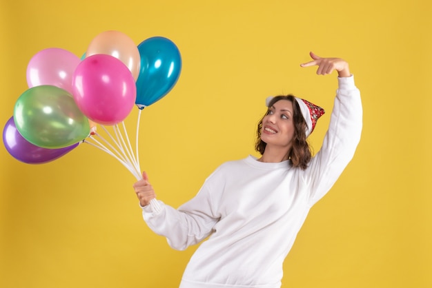 Vooraanzicht jonge mooie vrouw met kleurrijke ballonnen op gele kleur Kerstmis Nieuwjaar emotie vrouw