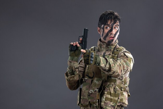 Vooraanzicht jonge soldaat die zich in camouflage met pistool op donkere muur overgeeft