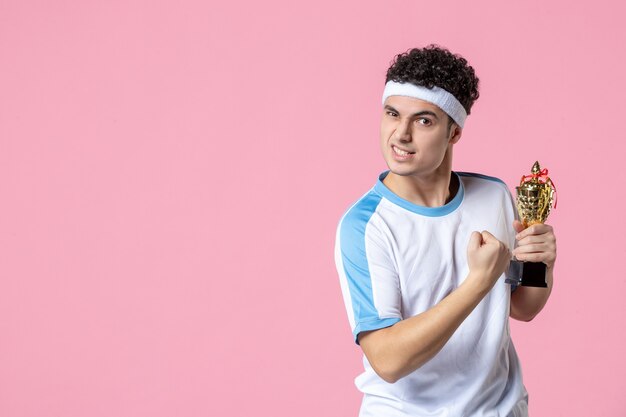 Vooraanzicht jonge speler in sportkleren met gouden kop op roze muur