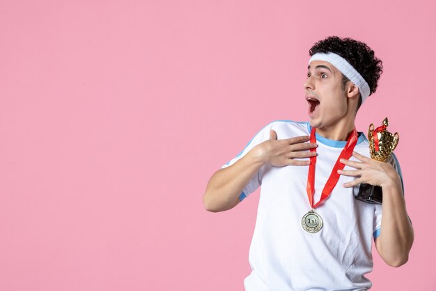 Vooraanzicht jonge speler in sportkleren met gouden kop op roze muur