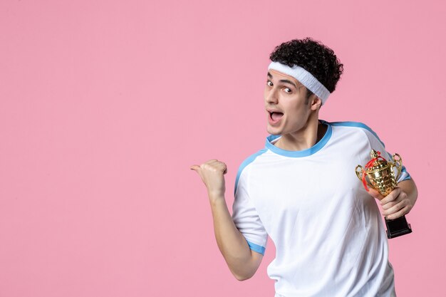 Vooraanzicht jonge speler in sportkleren met gouden kop op roze muur
