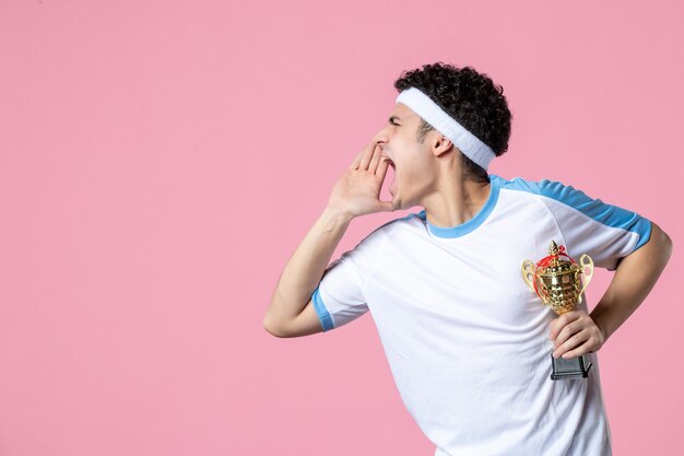 Vooraanzicht jonge speler in sportkleren met gouden kop op roze muur