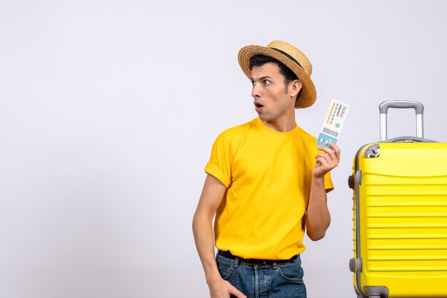 Vooraanzicht jonge toerist in geel t-shirt staande in de buurt van gele koffer kijken naar linker kaartje te houden