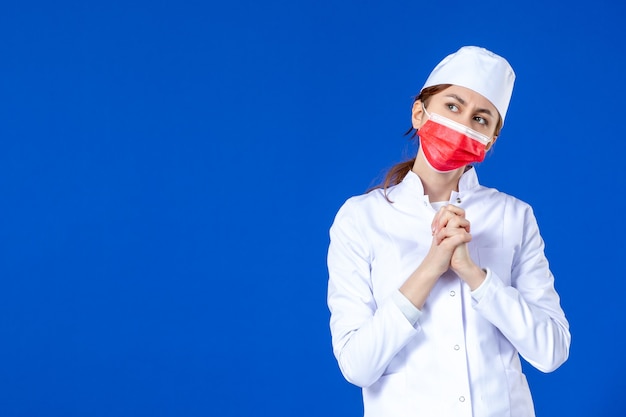 Vooraanzicht jonge verpleegster in medisch pak met rood masker op blauwe muur