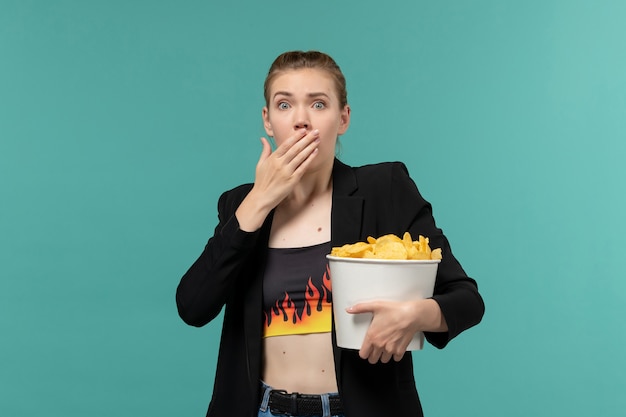 Vooraanzicht jonge vrouw aardappel chips eten kijken naar film op het blauwe oppervlak