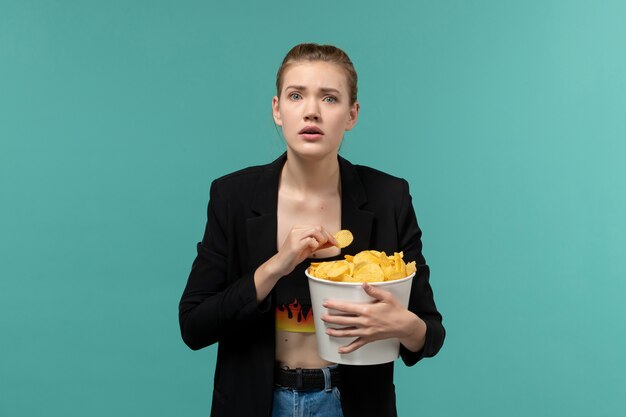 Vooraanzicht jonge vrouw aardappel chips eten kijken naar film op het lichtblauwe oppervlak