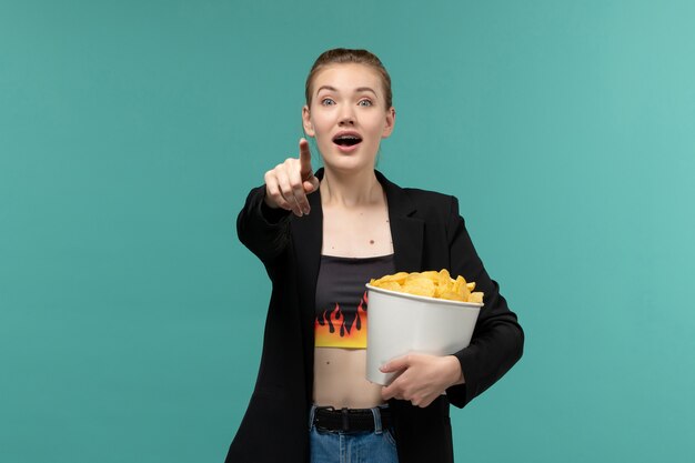 Vooraanzicht jonge vrouw aardappel cips eten en kijken naar film op blauwe ondergrond