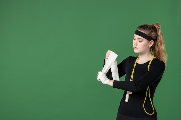 Vooraanzicht jonge vrouw die haar arm vastbindt met verband op groene achtergrond atleet training flex gezondheid vrouw sport lichaam