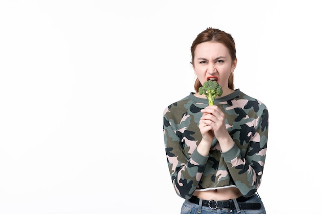 Vooraanzicht jonge vrouw die kleine groene broccoli vasthoudt en bijt op een witte achtergrond schotel lunch lichaam gezondheid voedsel horizontale salade maaltijd dieet