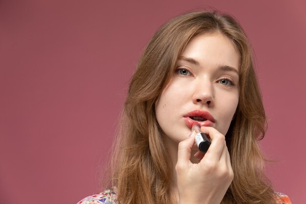 Vooraanzicht jonge vrouw die lippenstift gebruikt en rechtstreeks bekijkt