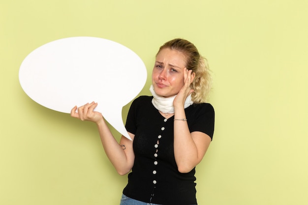 Gratis foto vooraanzicht jonge vrouw die zich erg ziek en ziek voelt met een groot wit bord benadrukt op de groene muur ziekte geneeskunde gezondheid ziekte