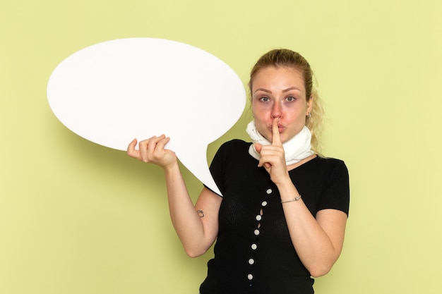 Gratis foto vooraanzicht jonge vrouw die zich erg ziek en ziek voelt met een groot wit bord met de vraag om stil te zijn op de groene muur ziekte geneeskunde gezondheid ziekte