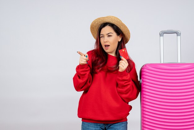 Vooraanzicht jonge vrouw die zich voorbereidt op een reis en een bankkaart op een witte muur houdt