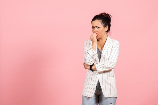 Vooraanzicht jonge vrouw, gekleed in witte jas met nerveus gezicht op roze achtergrond dame mode vrouw emotie kleur