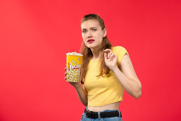 Vooraanzicht jonge vrouw in bioscoop houden popcorn pakket op rode muur films theater bioscoop snack vrouwelijke leuke film