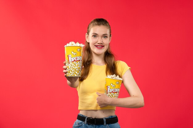 Vooraanzicht jonge vrouw in bioscoop met popcornpakket op de lichtrode muur bioscoop bioscoop vrouwelijke leuke film