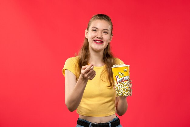 Vooraanzicht jonge vrouw in bioscoop popcorn houden en lachen op de rode muur bioscoop bioscoop vrouwelijke leuke film