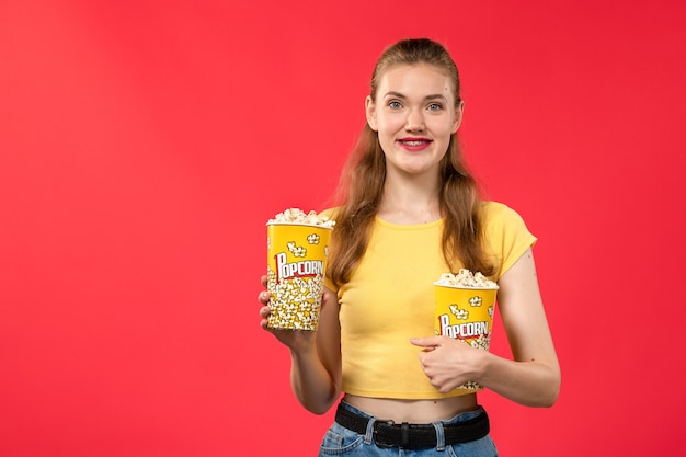 Vooraanzicht jonge vrouw in bioscoop popcorn houden en lachend op rode muur bioscoop bioscoop vrouwelijke leuke film