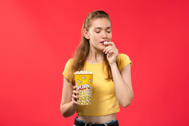 Vooraanzicht jonge vrouw in bioscoop popcorn pakket houden en eten op rode muur films theater bioscoop film