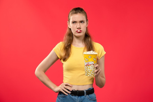 Vooraanzicht jonge vrouw in bioscoop popcorn pakket houden en poseren op rode muur films theater bioscoop vrouwelijke leuke film