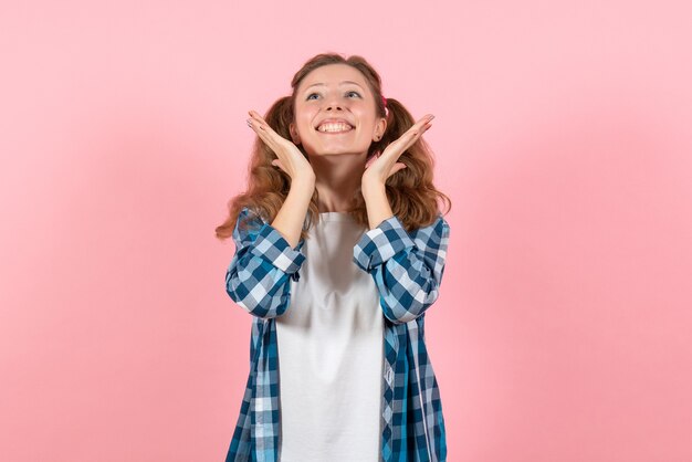 Vooraanzicht jonge vrouw in blauw geruit overhemd poseren met lichte glimlach op roze achtergrond vrouw emoties model mode meisjes kleur