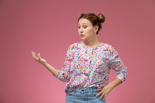 Vooraanzicht jonge vrouw in bloem ontworpen shirt en spijkerbroek poseren met opgeheven hand op de roze achtergrond