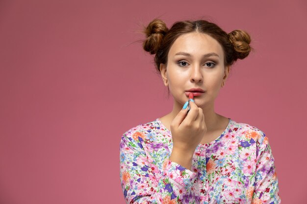 Vooraanzicht jonge vrouw in bloem ontworpen shirt en spijkerbroek schilderen haar lippen op de roze achtergrond