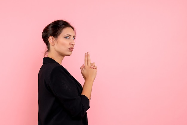 Vooraanzicht jonge vrouw in donkere jas in pistool houden pose op roze achtergrond