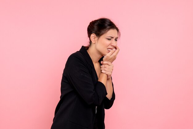 Vooraanzicht jonge vrouw in donkere jas met kiespijn op roze achtergrond