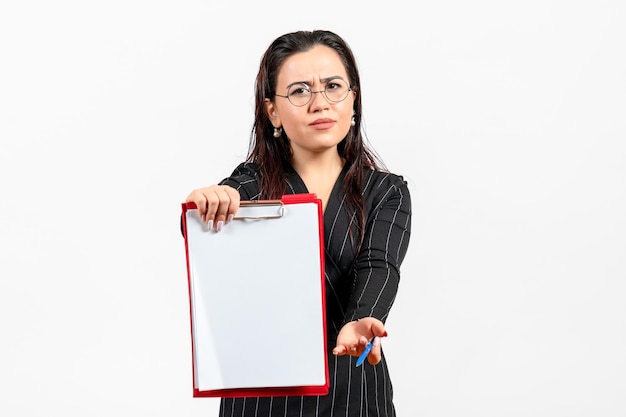 Vooraanzicht jonge vrouw in een donker streng pak die rood bestand op witte achtergrond suggereert, zakelijke vrouwelijke kantoordocumenttaak