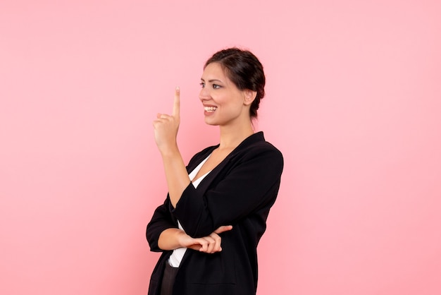 Vooraanzicht jonge vrouw in een donkere jas lachend op de roze achtergrond