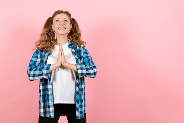 Gratis foto vooraanzicht jonge vrouw in geruit overhemd poseren en bidden op roze achtergrond vrouw jeugd kleur emoties kind model