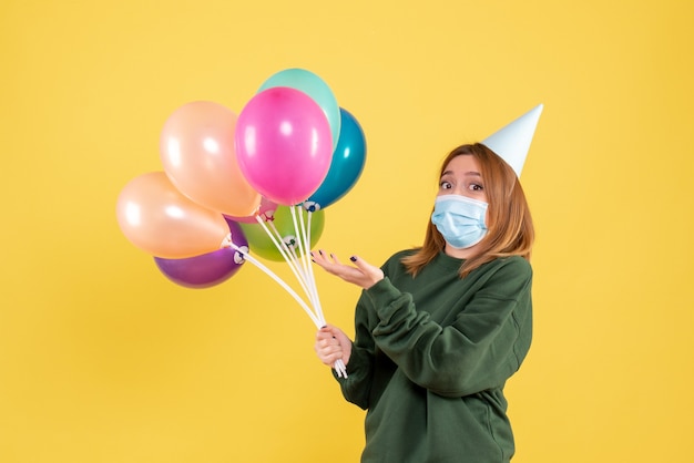 Vooraanzicht jonge vrouw in masker met kleurrijke ballonnen