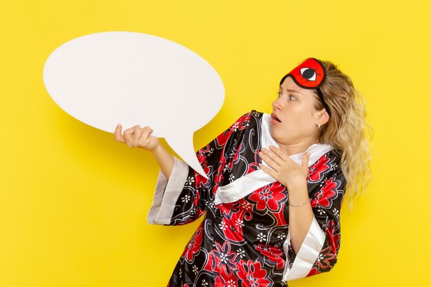 Vooraanzicht jonge vrouw in nachtjas met groot wit bord op gele muur slaap nacht bed model kleur