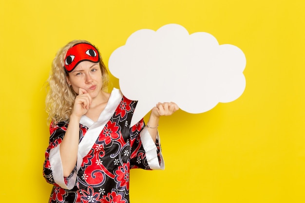 Vooraanzicht jonge vrouw in nachtjas oogmasker met groot wit bord denken aan gele muur slaap nacht bed model kleur