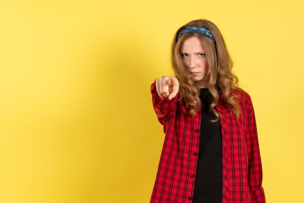 Vooraanzicht jonge vrouw in rood geruit overhemd permanent en wijzend op gele achtergrond kleur vrouw model menselijk meisje