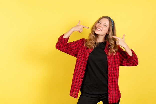 Vooraanzicht jonge vrouw in rood geruit overhemd poseren met glimlach op gele achtergrond menselijke meisjes emotie kleur model vrouw