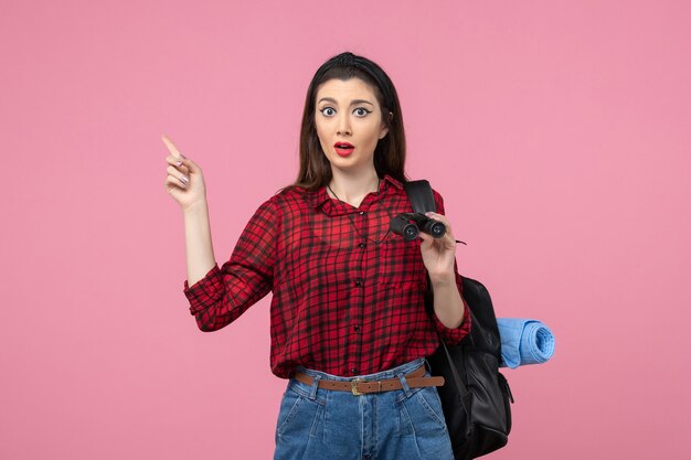 Vooraanzicht jonge vrouw in rood shirt met een verrekijker op de roze achtergrond vrouw kleur student