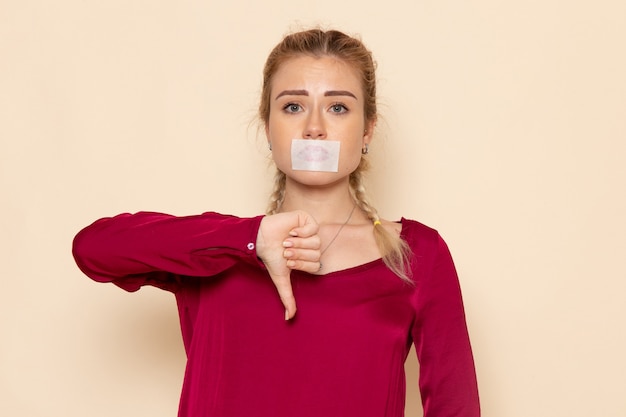 Vooraanzicht jonge vrouw in rood shirt met gebonden mond op de crème ruimte vrouwelijke doek foto geweld huiselijk