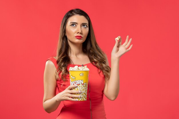 Vooraanzicht jonge vrouw in rood shirt met popcorn op het rode oppervlak