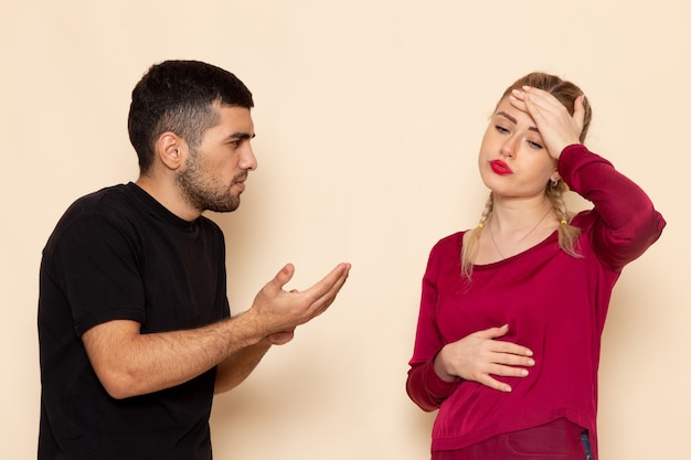 Gratis foto vooraanzicht jonge vrouw in rood shirt quarelling met jonge man op de crème ruimte vrouwelijke doek quarell confrontatie