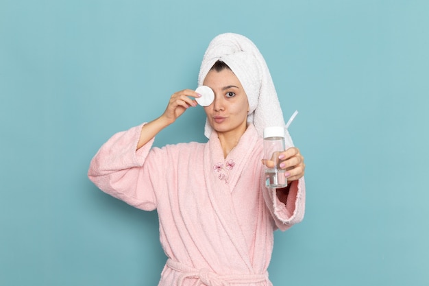 Vooraanzicht jonge vrouw in roze badjas die haar gezicht van make-up op de blauwe muur schoonmaakt