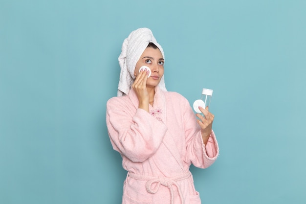 Gratis foto vooraanzicht jonge vrouw in roze badjas haar gezicht van make-up op blauwe muur schoonmaken schoonheid schoon water zelfzorg crème douche